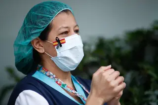 Una sanitaria, con una mascarilla que muestra una bandera de España con un lazo negro de luto por los fallecidos por coronavirus, aplaude en agradecimiento por el homenaje a los Sanitarios del Hospit