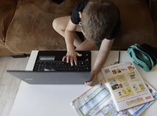 Un alumno de Primaria haciendo los deberes de la asignatura de Inglés con varios libros y un ordenador
