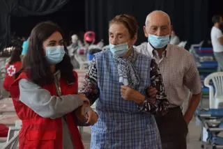 Una voluntaria de Cruz Roja ayuda a dos ancianos desalojados por el incendio en Ifeza