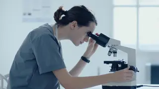 Investigadora mirando por un microscopio MICIU. Patentes.