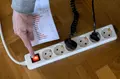 Un hombre enciende una alargadera con varios enchufes con una factura de luz en la mano