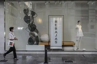 Una mujer protegida con mascarilla pasa al lado del escaparate de una tienda donde se observan carteles indicativos de rebajas en Valencia, Comunidad Valenciana (España)
