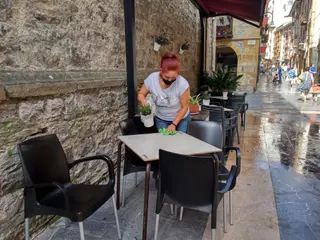 Una trabajadora desinfecta la mesa de la terraza de uno de los locales hosteleros que han vuelto a la fase 2 tras las limitaciones impuestas por el Gobierno Vasco. En Ermua, Vizcaya, País Vasco, (Esp