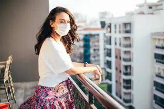 Mujer con mascarilla mira desde el balcón durante el confinamiento por el coronavirus.